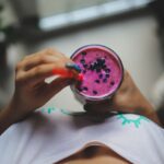 The image shows a woman's hand holding a purple smoothie in a glass. The post is how to be a healthy vegan